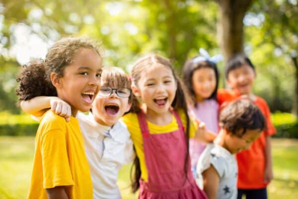 A group of six children laughing together outdoors, with trees and sunlight in the background, echoes the vibrant spirit nurtured by the Guaranty Foundation.