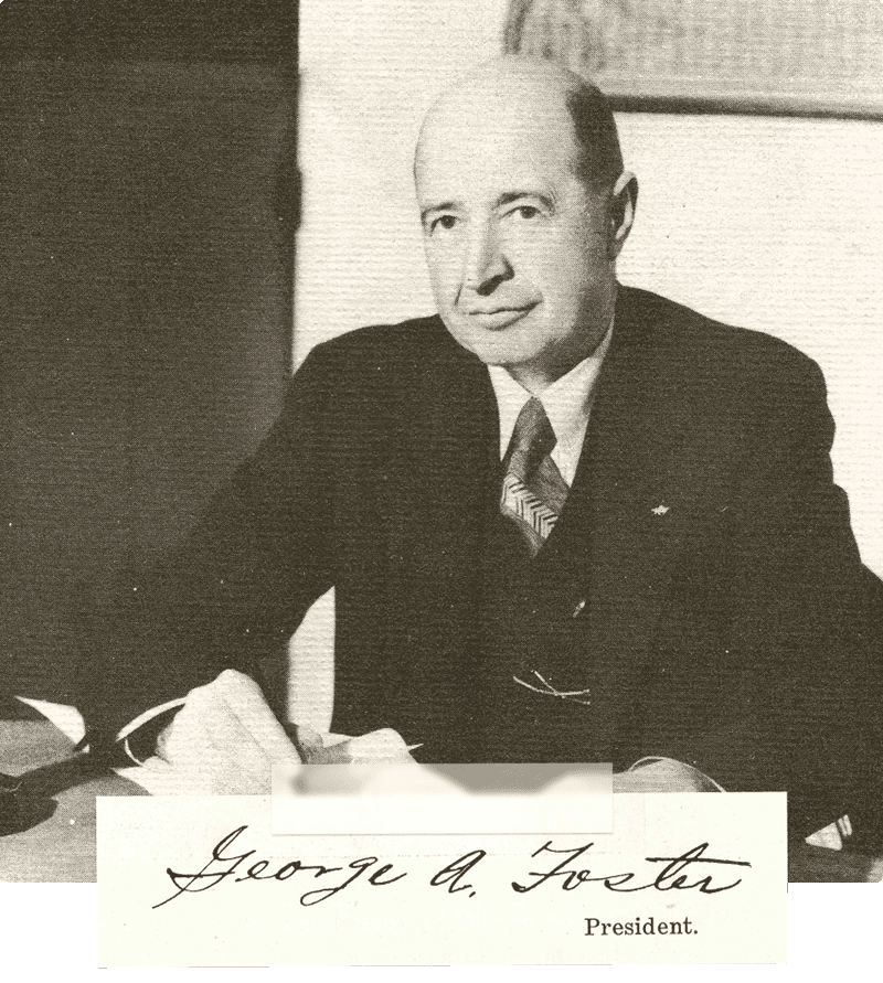 George Foster Sr. sits at a desk, holding a pen. His signature and the title 