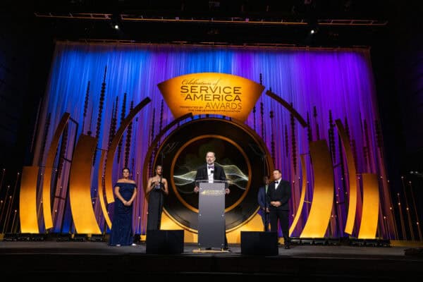 Flynn Foster speaks at a podium on a stage with a 