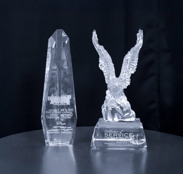 Two crystal awards on a table: one tall and pointed, the other shaped like an eagle with wings spread.