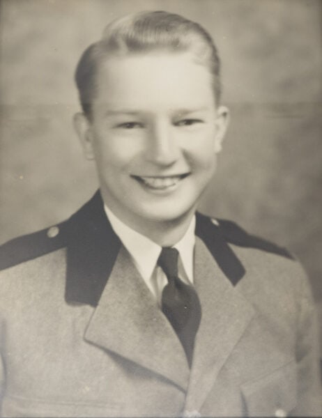 Black and white portrait of a young person, George Foster, wearing a formal suit and tie, smiling at the camera, capturing the essence of Baton Rouge Radio Station's vibrant spirit.