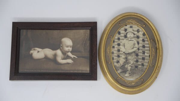 Two framed vintage photographs of George A. Foster Sr.: left, a baby lying on its stomach; right, a young child standing against a brick wall, wearing a hat and holding an object.