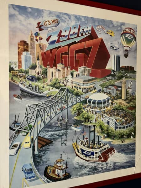 An illustration showcasing a vibrant cityscape with a bridge, riverboat, and hot air balloon. The iconic WGG7 logo of Guaranty Media proudly features, capturing the spirit of Baton Rouge's premier radio station.