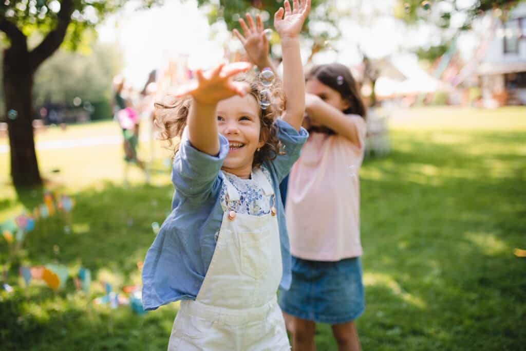 Two children play outside with bubbles on grass in sunny weather